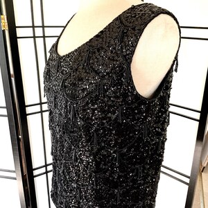 May include: A black sleeveless top with a sequined design. The sequins are arranged in a pattern of small, overlapping circles. The top has a scoop neckline and a loose fit.