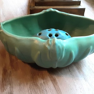 May include: A vintage, seafoam green ceramic flower frog and bowl. The bowl has a scalloped edge and a central insert with multiple holes for arranging flowers. The flower frog is a lighter shade of blue.