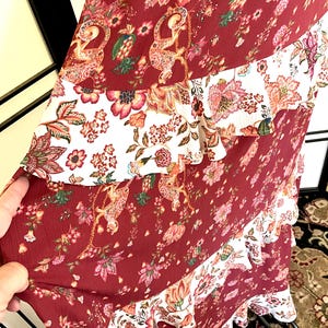 Pode incluir: Um vestido maxi comprido, cor vinho, com estampa floral branca e vinho. O vestido tem uma saia em camadas com babados e um corpete justo.