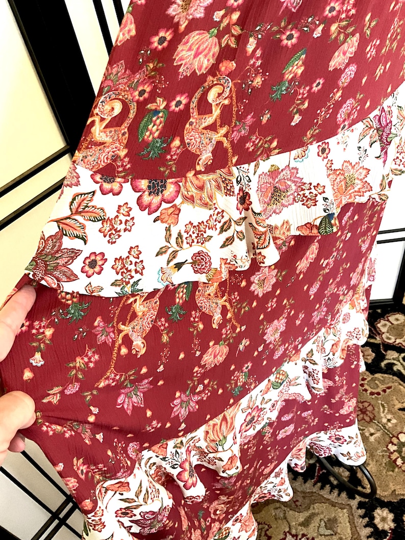 Pode incluir: Um vestido maxi comprido, cor vinho, com estampa floral branca e vinho. O vestido tem uma saia em camadas com babados e um corpete justo.