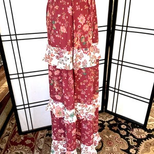Pode incluir: Uma saia longa e em camadas com estampa floral. A saia &eacute; feita de um tecido macio e fluido e tem uma bainha com babados. A saia &eacute; de cor bord&ocirc; escura com detalhes florais brancos e rosados.