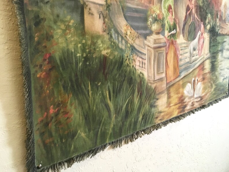 May include: A tapestry featuring a garden scene with a stone building, a pond, and two swans. The tapestry is predominantly green, brown, and white and has a fringed border.