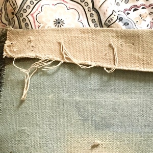 May include: Close-up of the back side of a light blue throw blanket with a tan fabric border. The border has loose threads and is frayed in places.