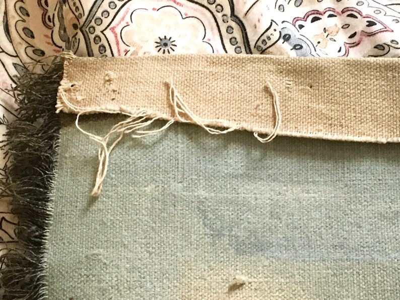 May include: Close-up of the back side of a light blue throw blanket with a tan fabric border. The border has loose threads and is frayed in places.