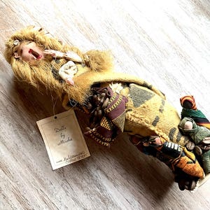 May include: A handmade doll with long blonde hair, wearing a brown and yellow patterned dress. The doll is holding a smaller doll in its arms. The doll is labeled "Dolls by Mischa" and "Limited Edition Collector's Edition".