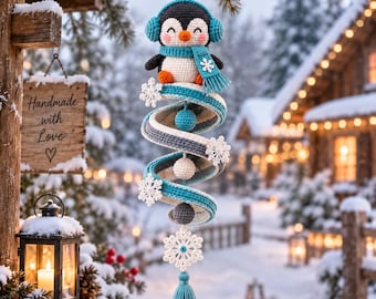May include: A crochet hanging ornament featuring a penguin wearing blue earmuffs and a matching scarf. The penguin sits atop a spiral structure in shades of blue, white, and gray, decorated with white snowflake accents and small spheres, ending in a blue tassel.