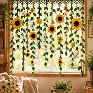 Könnte beinhalten: Ein handgefertigter Häkel-Fensterbehang mit hängenden grünen Ranken, gelben Sonnenblumen und kleinen weißen Blüten. Der Vorhang ist an einer Holzstange befestigt und zeigt ein komplexes grünes Gittermuster oben sowie lange, herabhängende Blattstiele.