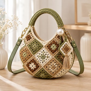 May include: A crescent-shaped handbag crafted from crocheted granny squares in shades of olive green, cream, and brown. The bag features a thick crocheted handle, a detachable green strap, a large white pearl charm, and a small matching tassel.