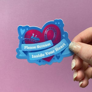 May include: A blue and red heart-shaped sticker with a roller coaster inside. The sticker has the text "Please Scream Inside Your Heart" on it.