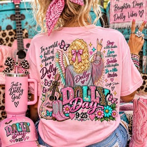May include: A light pink t-shirt featuring a graphic of a blonde figure with wings, a guitar, and cowboy boots. Text includes In a world full of ordinary be a Dolly, Dolly Day 9:25, and Sing a little louder, Love a little bigger, Sparkle a little brighter.