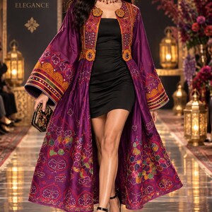 May include: A long-sleeved purple duster coat featuring intricate multi-colored embroidery and circular orange accents, worn over a simple black mini dress. The garment includes wide sleeves with detailed patterns and a structured bodice design.