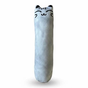 May include: A long, cylindrical plush toy in a soft light gray color. The top features embroidered black details depicting a cat face with closed eyes, a small nose, and whiskers. The fabric has a smooth, velvety texture throughout the body.