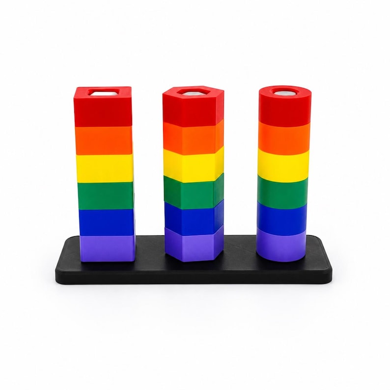 Op de afbeelding: Een houten speelgoedset met drie verticale kolommen op een zwarte rechthoekige basis. Elke kolom bestaat uit vijf gestapelde blokken in regenboogkleuren: rood, oranje, geel, groen, blauw en paars. De vormen zijn vierkant, zeshoekig en cirkelvormig.