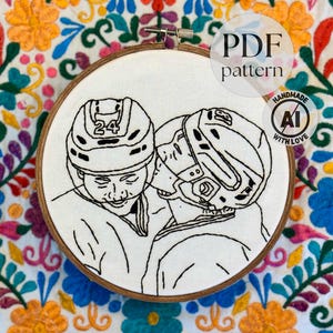 May include: A hand-stitched embroidery hoop featuring a black line drawing of two hockey players wearing helmets. One helmet has the number 24. The text "PDF pattern" and "Handmade with Love" are also visible.
