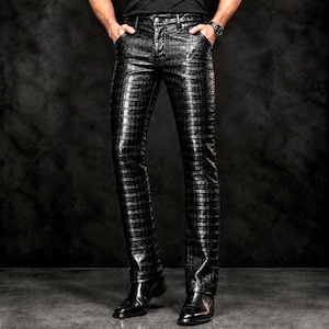 May include: Black trousers featuring a glossy, embossed crocodile skin texture. These trousers include a standard button and zip fly closure, front pockets, and a straight-leg cut. The material has a reflective finish with a grid-like pattern.