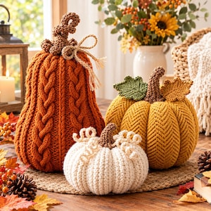 May include: Three decorative pumpkins made of knit yarn. One tall orange pumpkin with a cable knit pattern and a jute twine bow, one round yellow pumpkin with a herringbone knit pattern and two knit leaves, and one small white ribbed pumpkin.