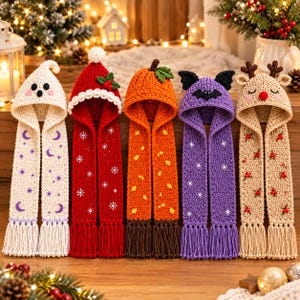 May include: Five crochet hooded scarves with fringe. The designs include a white ghost with purple moons, a red Santa hat with snowflakes, an orange pumpkin with leaves, a purple bat with stars, and a tan reindeer with red berries.