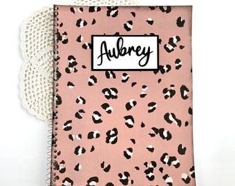 May include: A pink spiral notebook with a leopard print design and the name "Aubrey" printed on the front in black.