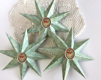 May include: Three teal blue paper stars with a vintage Santa Claus image in the center of each star. The stars are layered on top of each other and are on a white crocheted doily.