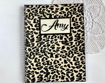 May include: A black and white leopard print spiral notebook with the name "Amy" written in black cursive on a white label.
