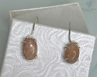 May include: A pair of silver earrings with pink oval-shaped stones. The earrings are handmade and feature a simple design.