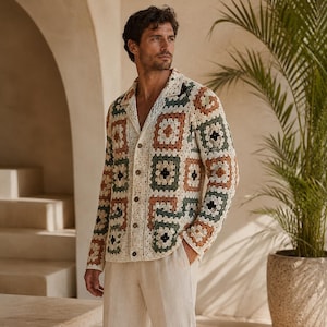 May include: A long-sleeved button-down cardigan featuring a multi-colored granny square crochet pattern in shades of cream, olive green, and terracotta. The garment has a collared neckline, a front button closure, and two patch pockets on the front.