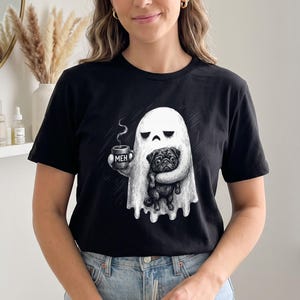 Könnte beinhalten: Ein schwarzes Kurzarm-T-Shirt mit einer weißen Grafik eines Geistes, der eine Tasse mit der Aufschrift MEH hält und einen schwarzen Mops umarmt. Das Design ist mittig auf der Brust platziert und zeigt eine detaillierte Illustration.