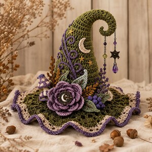 Puede incluir: Un sombrero puntiagudo de ganchillo en color verde oliva con la punta curvada, decorado con una flor morada grande, una luna creciente, estrellas pequeñas, una seta y colgantes. El ala presenta un borde ondulado en beige claro y morado.