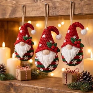 May include: Three crocheted gnome ornaments hanging by twine. Each gnome features a red pointed hat with white snowflake embroidery, a white yarn beard, a beige nose, and a round body with red and green stripes accented by white snowflakes.