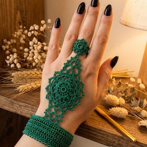 May include: A dark green crochet hand ornament featuring a wide wristband with integrated beads and a central lace motif that extends upward to connect to a matching crochet ring, creating a decorative piece that covers the back of the hand.