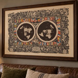 Op de afbeelding: Een ingelijste rechthoekige wandkaart getiteld The World of Ours, met twee cirkelvormige zwart-wit hemisferen omringd door een rand van kleurrijke internationale vlaggen en gedetailleerde zwart-wit illustraties van figuren en mythische wezens.