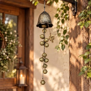 May include: A hanging wind chime featuring a dark, textured bell at the top, from which a vertical string of multiple small, spherical, gold-toned filigree bells is suspended. A single gold-toned metal leaf charm hangs from a short chain.