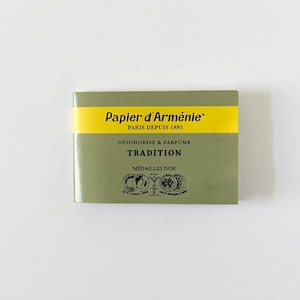 Può includere: Un libretto rettangolare di carta d'Armenia Papier d'Arménie con una copertina verde oliva. Una fascia gialla orizzontale presenta il testo nero Papier d'Arménie PARIS DEPUIS 1885. Sotto, il testo recita DÉSODORISE & PARFUME TRADITION MÉDAILLES D'OR.