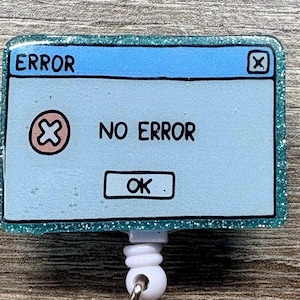 May include: A rectangular badge reel featuring a light blue computer error message graphic with the text ERROR, NO ERROR, and OK. The frame is a glittery teal color with a white plastic retractable cord mechanism attached to the bottom center.