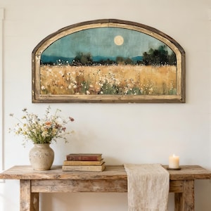May include: A rustic wooden console table with a vase of flowers, books, and a candle. Above, a framed landscape painting depicts a field under a moonlit sky. The painting is in a distressed wooden frame.