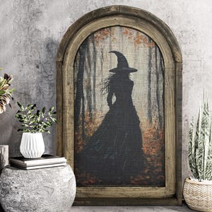 May include: A framed canvas print of a witch in a forest setting. The witch is silhouetted against a backdrop of trees and leaves. The frame is made of wood and has a rustic finish.