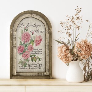 May include: A rustic wooden sign with a distressed white background featuring a floral design and the text "Le Boutique de Fleurs".