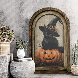 May include: A framed Halloween-themed artwork features a black cat wearing a witch's hat, perched atop an orange jack-o'-lantern. The artwork is set within a rustic, arched wooden frame, creating a vintage aesthetic. The background is a neutral beige, enhancing the colors of the cat and pumpkin.