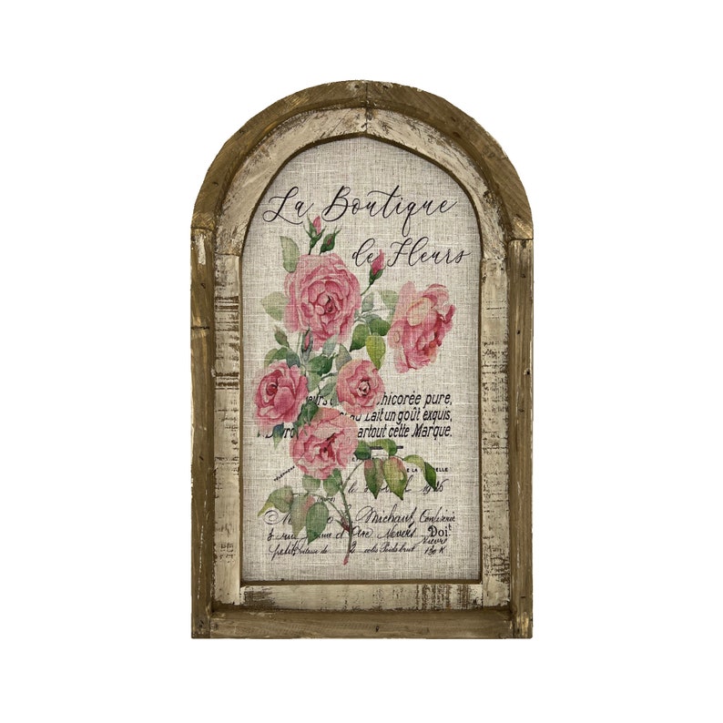May include: A rustic wooden framed sign with a white background and a floral design. The sign reads "La Boutique de Fleurs" and features pink roses with green leaves. The sign has a distressed, vintage look.