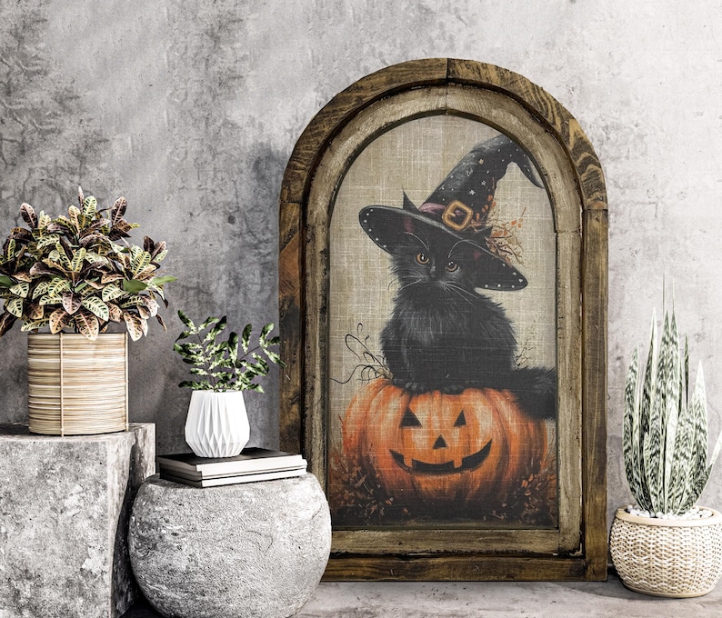 May include: A framed Halloween-themed artwork features a black cat wearing a witch's hat, perched atop an orange jack-o'-lantern. The artwork is set within a rustic, arched wooden frame, creating a vintage aesthetic. The background is a neutral beige, enhancing the colors of the cat and pumpkin.
