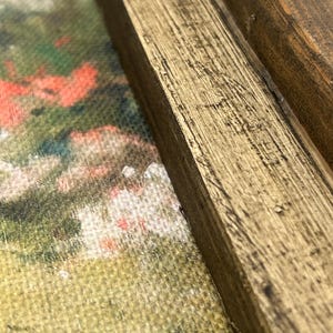 May include: Close-up of a framed painting with a gold-painted wooden frame. The artwork features a colorful, impressionistic landscape with red, green, and white hues. The frame has visible wood grain and a distressed finish.