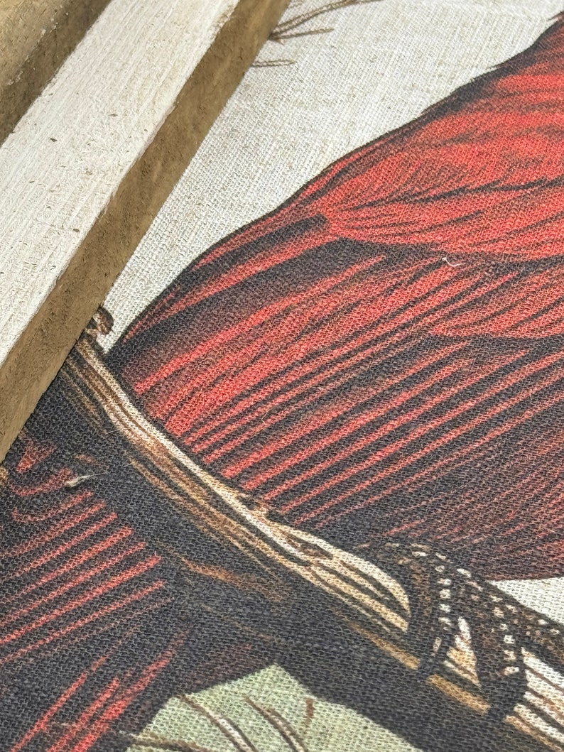 May include: Close-up of a red cardinal bird with black and white markings on its wings, perched on a branch. The bird is depicted on a canvas with a textured linen-like surface.