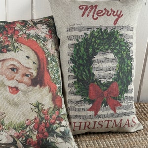 May include: Two decorative throw pillows with a Christmas theme. One pillow features a vintage illustration of Santa Claus with holly and berries. The other pillow has a green wreath with a red bow on a background of sheet music with the words "Merry Christmas".