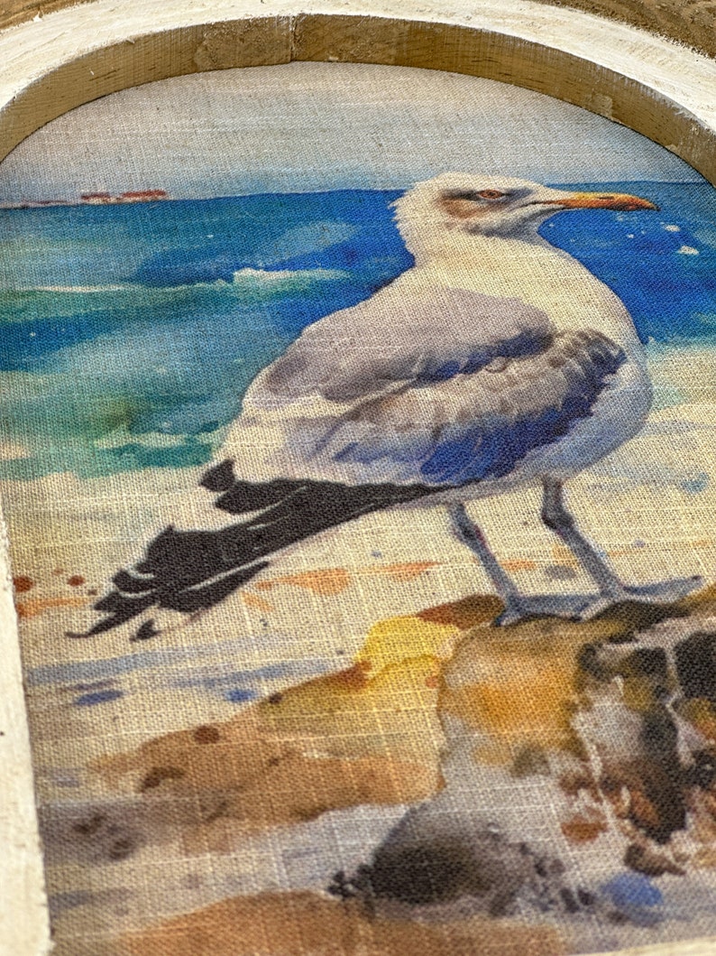 Op de afbeelding: Een aquarel schilderij van een meeuw die op een rots zit met de oceaan op de achtergrond. De meeuw is wit met zwarte vleugels en een gele snavel. De oceaan is blauw met witte golven. De rots is bruin en heeft een textuur.