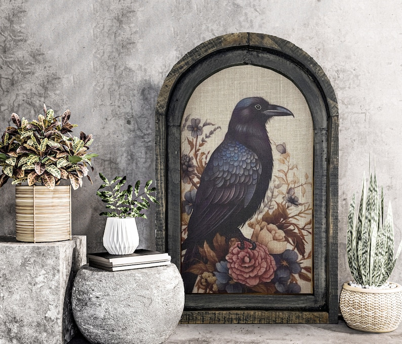 May include: A framed canvas print with a black raven perched on a branch of flowers. The raven has blue feathers and is surrounded by pink, red, and white flowers. The frame is dark brown wood with a distressed finish.