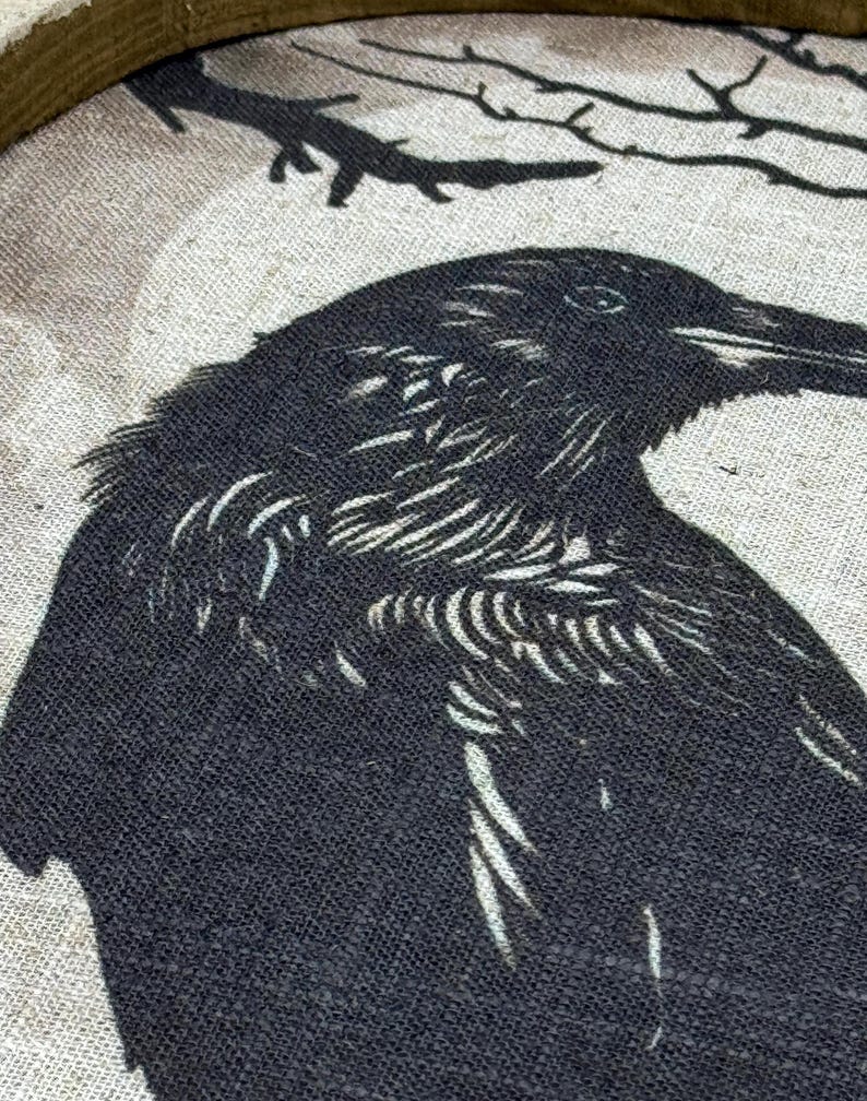 May include: A black crow with a detailed, textured design is printed on a beige canvas background. The crow is facing the right side of the image and has a sharp beak. The background is a light beige with a subtle texture.