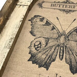 May include: A framed burlap canvas with a black and white butterfly illustration. The canvas has the text "Butterfly" and "Le Papillon" printed on it.