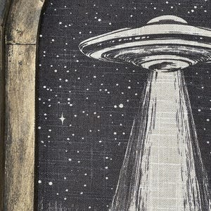 May include: A black and white illustration of a UFO with a beam of light shining down on a field of grass. The UFO is against a black background with white stars.