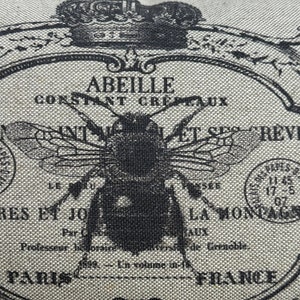 May include: A black and white illustration of a bee with the text "Abeille Constant Cretaux" and "Int. Nat. et Ses Revues" on a beige fabric background.