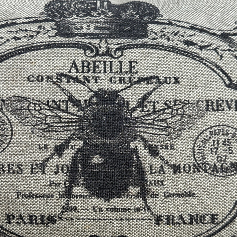 May include: A black and white illustration of a bee with the text "Abeille Constant Cretaux" and "Int. Nat. et Ses Revues" on a beige fabric background.